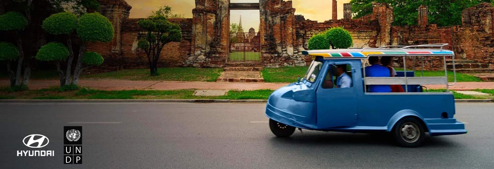 Camioneta azul antigua circulando junto a ruinas arqueológicas