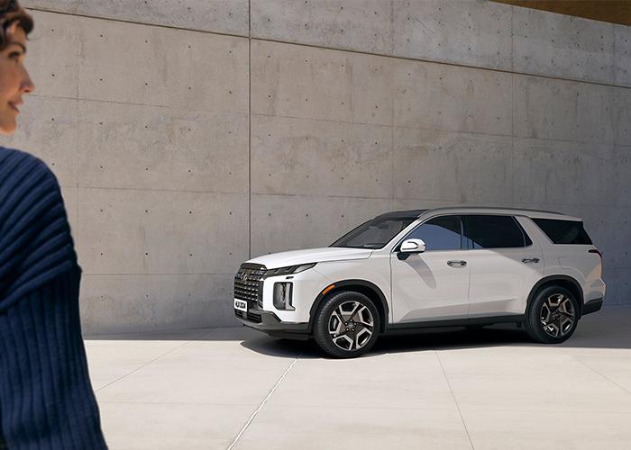 Mujer en primer plano con una Hyundai Palisade color blanco en el frente