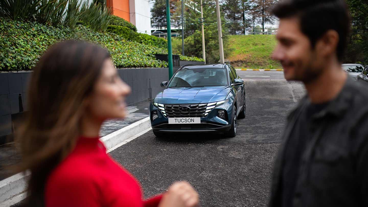 Pareja de personas desenfocadas en primer plano con Hyundai Tucson de fondo